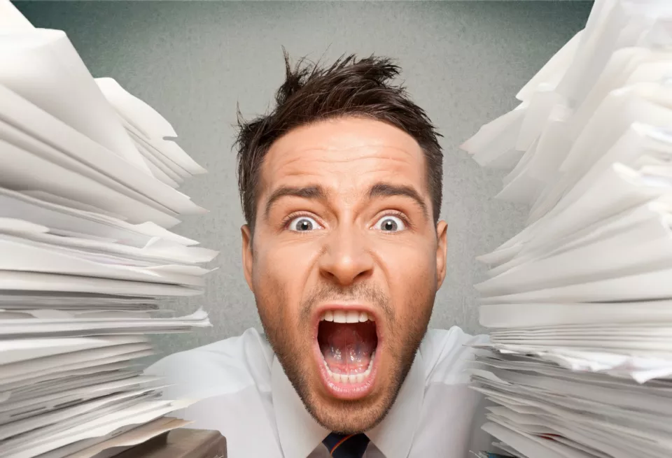 highly stressed man between piles of paperwork
